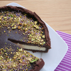 White and dark chocolate cheesecake decorated with chopped pistachios on black plate on wooden table
