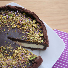 White and dark chocolate cheesecake decorated with chopped pistachios on black plate on wooden table
