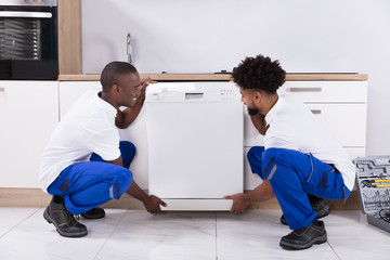 Two Handy Men Fixing The Dishwasher In The Kitchen