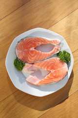 Fresh uncooked salmon fish slices with parsley on a plate on wooden background.