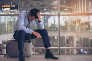 Businessman sitting on luggage at the  terminal airport alone, unhappy trip by delay flight....