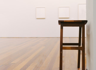 Wooden stool in empty museum looking room with paintings on wall