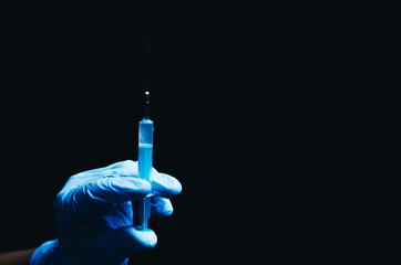 in the hand in a blue glove syringe on black background