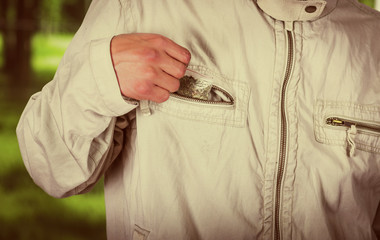 Close up of a man dealer saving in the pocket of his jacket drug, trafficking, crime, in a blurred background, vintage effect