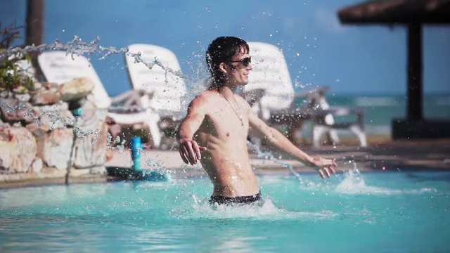 Young handsome man in sunglasses relaxing under the stream of water in swimming pool on travel vacation holidays. 1920x1080