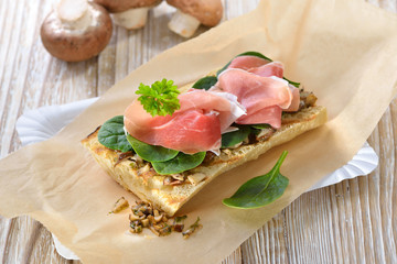 Heißes Ciabatta-Brot aus dem Grill belegt mit feinem Serrano Schinken, gebratenen Pilzen und jungem Spinat  - Street food: Toasted panini with Spanish ham, spinach leaves and fried mushrooms