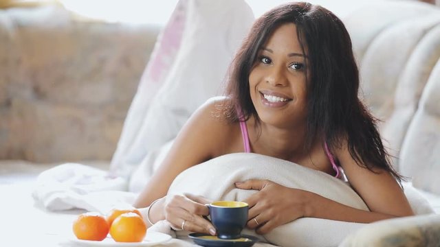Brunette woman in cosily bed drinking cup of tea at home