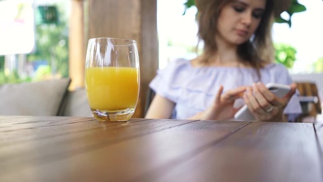 Glass of orange juice on backraund of young woman surfing internet in her smartphone