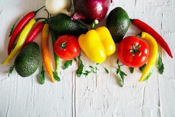 Collection fresh vegetables on a light background: tomatoes, peppers, chili, avocado, greens, onion. The concept of a natural healthy diet.