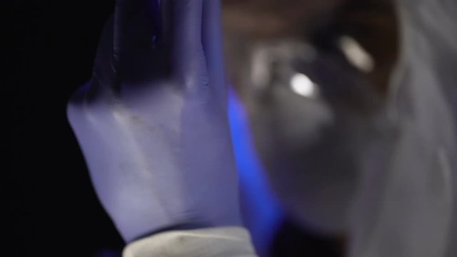 Lab scientist wearing exam gloves, reflection of test tubes in safety glasses