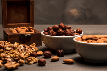 Two white cups with nuts, almonds, hazelnuts, walnut and a wooden box with almonds, side view