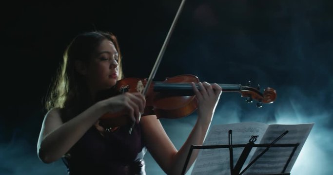 Violinist girl performing on stage, light, dark background
