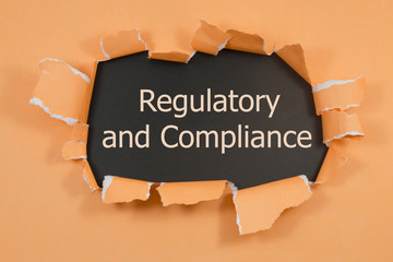 The text regulatory and compliance appearing behind torn paper