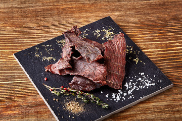 Dried peppered beef jerky cut in strips on the black board on wooden background