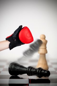 Hand of boxer knocking over chess piece