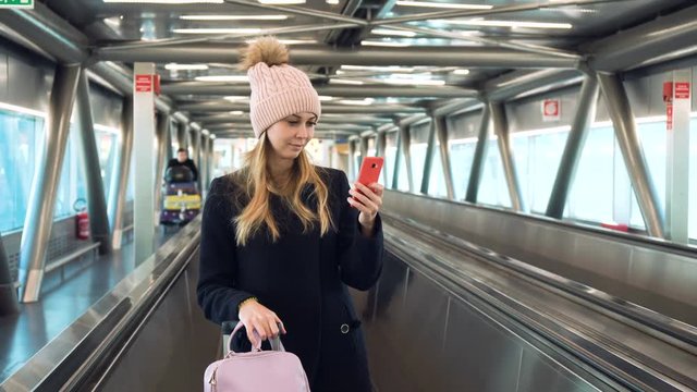 Young woman standing on escalator at the airport and using smartphone