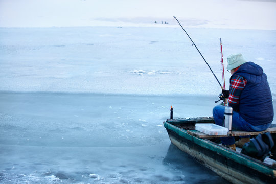 Back view o fisherman in boat while fishing in winter