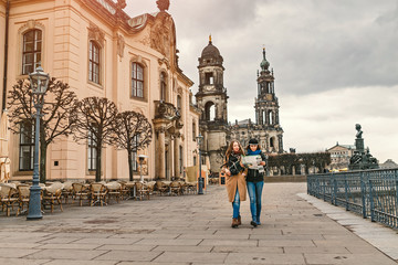 Obraz premium Two charming cheerful women are walking with a map along Dresden Street, Germany. The concept of love and friendship in travel