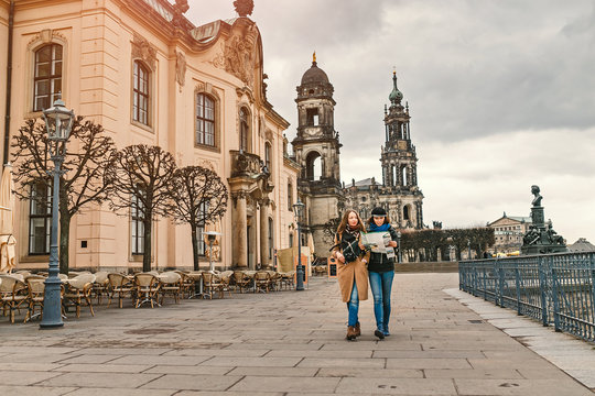 Two charming cheerful women are walking with a map along Dresden Street, Germany. The concept of love and friendship in travel