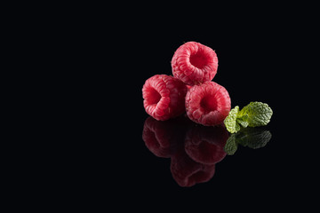 Fresh raw raspberry with mint leaf on the black glass background with a reflection