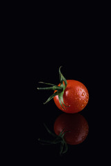 Cherry tomato with water drops on the black glass background
