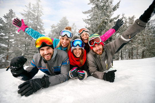 smiling friends on winter holidays - Skiers lying on snow and having fun