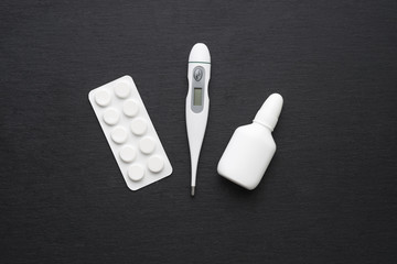 Thermometer, nasal drops and tablets on dark slate board. Flat lay. Meds for flue treatment, health care concept.
