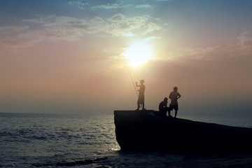 Fishermen on the beach in the evening on a sunset background. To fish. men's hobbies. Silhouette 