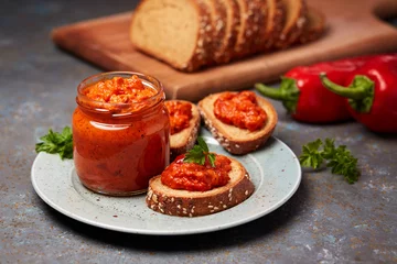Rolgordijnen Ajvar (pepper mousse) in a jar and on a slices of bread © Melica