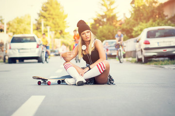Cool skater girl in street style, sitting on the street posing with skate board in urban environment © BigLike Images
