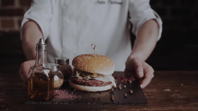 Chief cook preparing fresh burger in the kitchen.Burger restaurant menu cooking process. The cook puts ready parts of burger together. Fast food cafe cuisine. Selective focus. Modern color grade