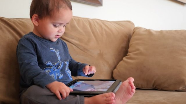 An adorable boy toddler playing with an ipad on the couch