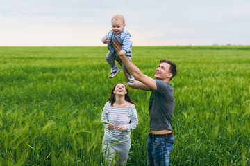 Joyful man, woman walk on green field background, rest, have fun, play, toss up little cute child baby boy. Mother, father, little kid son. Family day 15 of may, love, parents, children concept.