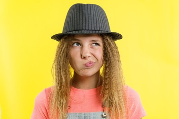 Pretty girl 12-13 years old blonde with curly hair in a hat, looks pensively aside, thinking about school.