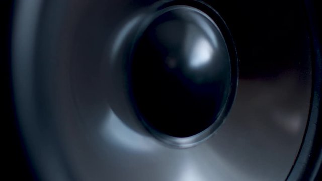 We move up a tower speaker to a vibrating woofer. It is pounding in a extreme close up.