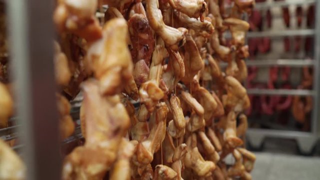 Smoked chicken and pork bacon hanging on racks in storage room at meat factory