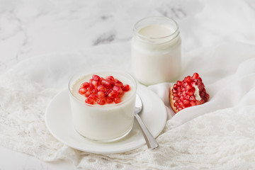Yogurt in a glass on a saucer with pomegranate seeds, lace napkin