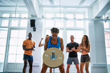 Woman weightlifting with friends encouraging her in the backgrou