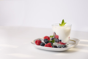 Closeup glass of yogurt with fresh berries and mint on the white plate on white background