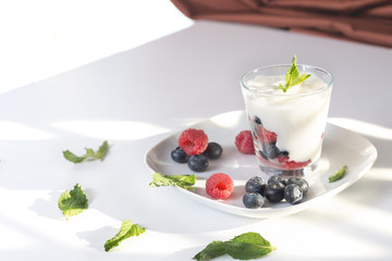 Closeup glass of yogurt with fresh berries and mint on the white plate. 