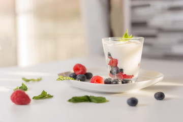 Glass of yogurt with fresh berries on blur home background. 