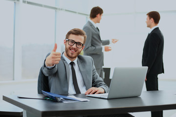 handsome young business man with people in background at office meeting. showing thumbs up.