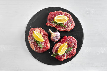 Fresh raw beef steaks with herbs, garlic, olive oil, pepper, salt and rosemary on black board: Tenderloin, Striploin, Rib Eye