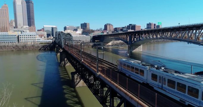 A slow forward aerial view of subway cars traveling on a railroad bridge over the Monongahela River in downtown Pittsburgh, PA.  	