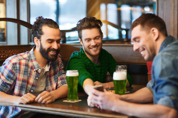 friends with smartphone drinking green beer at pub