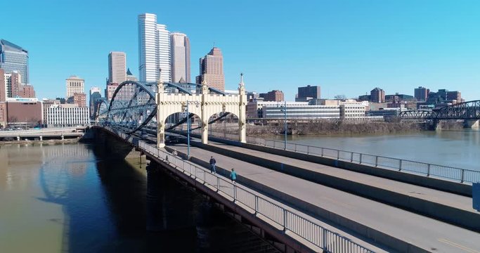 A slow forward aerial establishing shot of pedestrians and traffic on the Smithfield Bridge over the Monongahela River in downtown Pittsburgh, PA on a sunny winter day.  	