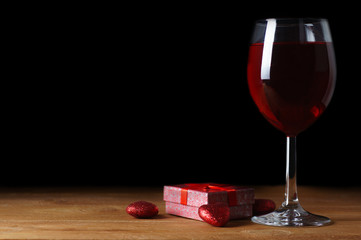 Gift for a holiday and a glass of red wine on a black background