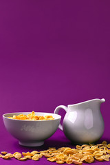 Bowl with corn flakes, jug of milk on purple background. Сoncept of a healthy breakfast