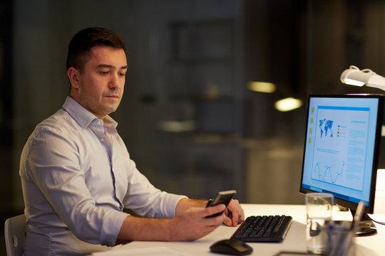 man with smartphone working late at night office