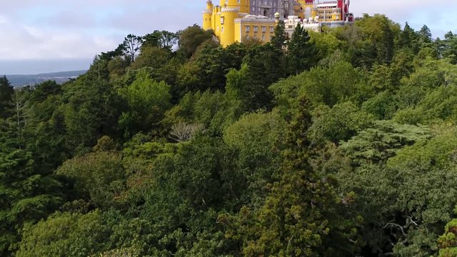 Aerial view of the iconic Pena National Palace moving up from forest originally built on Monastery of Nossa Senhora da Pena and renovated extensively through the initiative of Ferdinand II of Portugal